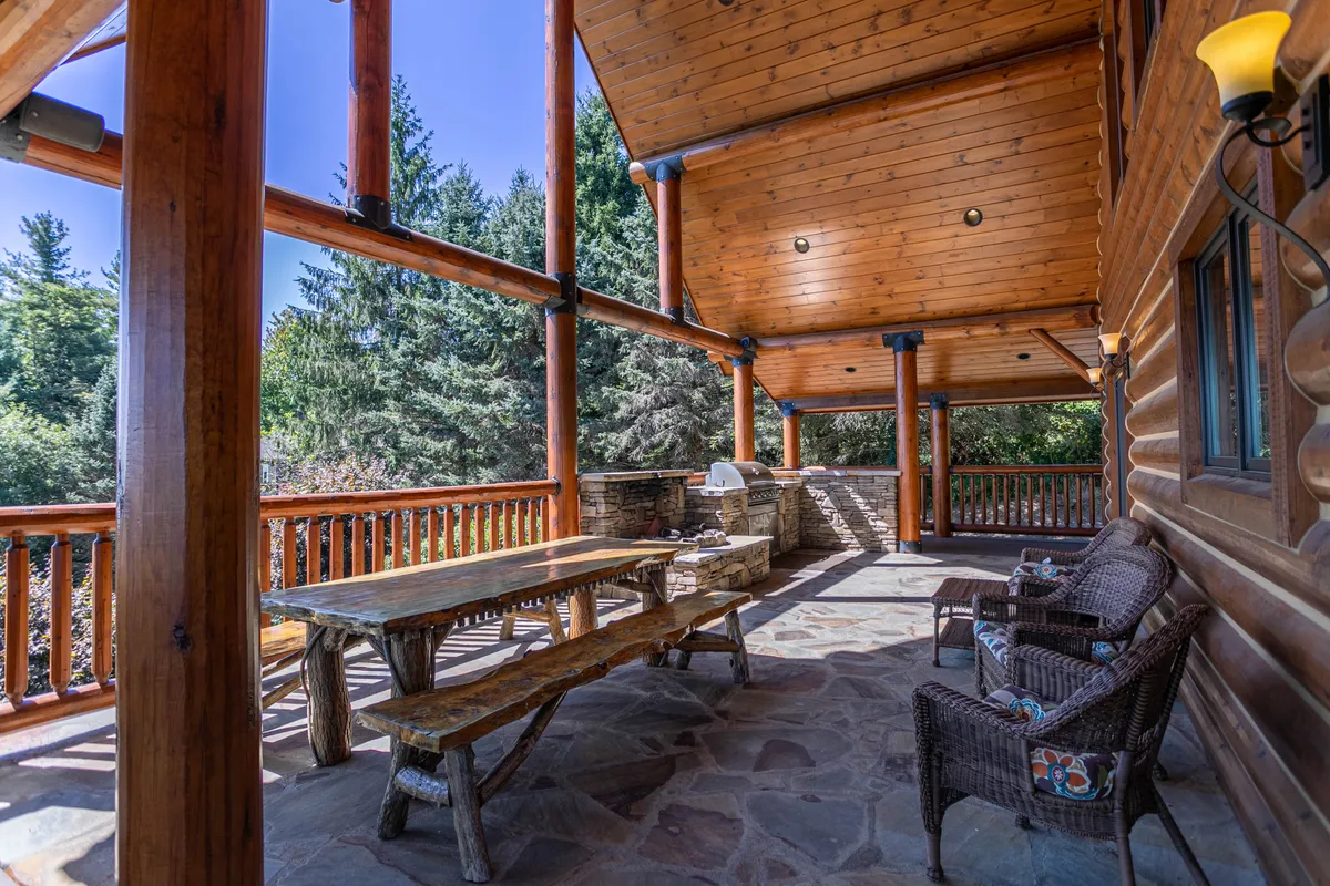 A large, rustic wooden dining table sits under the open sky, with rocking chairs and a stone grill set for outdoor dining. The setting is ideal for al fresco meals, social gatherings, and stargazing, embodying the estate’s blend of comfort and wellness in nature.