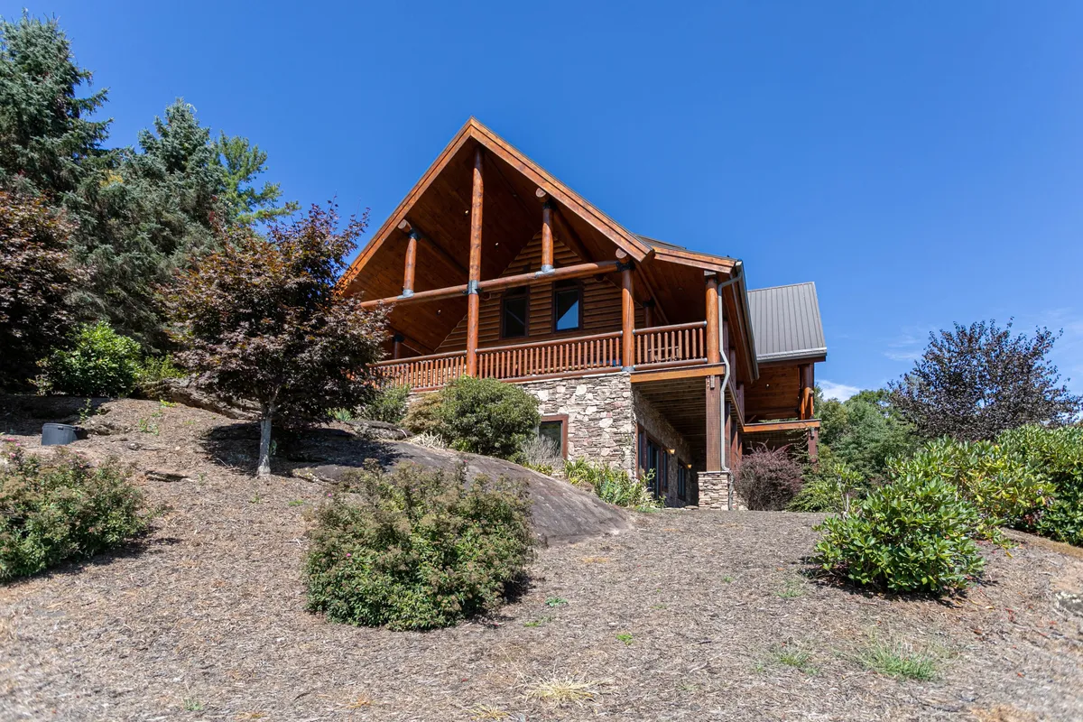 The inviting wooden beams and stone facade of the Lodge are featured prominently, with a sloped roof and open porch. The exterior design showcases classic mountain architecture and hints at the comforts waiting inside, while also framing the natural setting for sunset views or evening gatherings.
