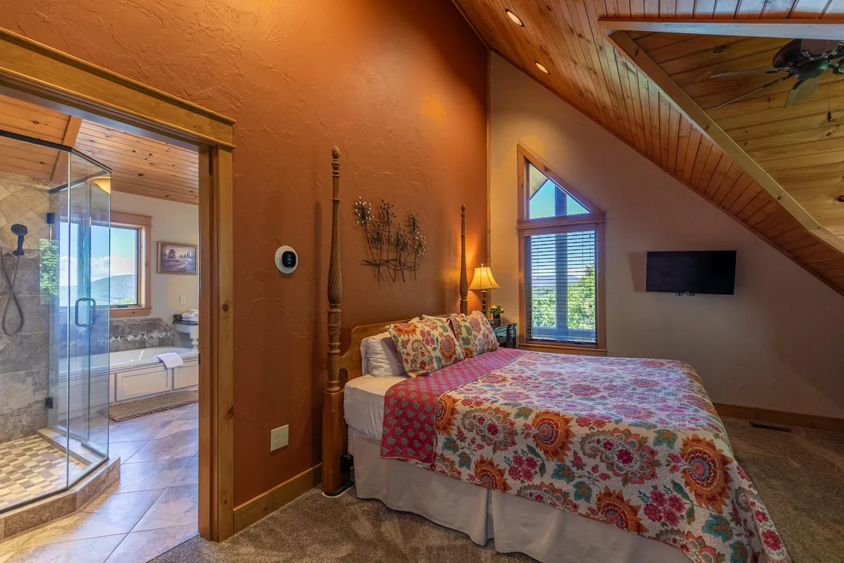 A tranquil bedroom with colorful bedding, a spacious shower area, a large window offering scenic views, and a wood-paneled ceiling. The atmosphere is serene and inviting, ideal for relaxation after a long day or enjoying quiet mornings.