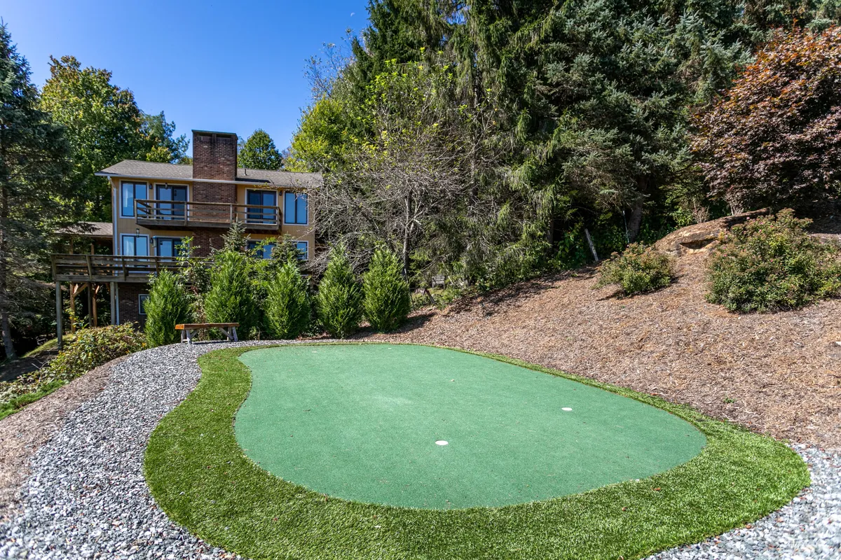 The back of the house features a well-maintained putting green surrounded by greenery, creating a playful and peaceful outdoor space. The scene suggests a spot for both exciting family golf games and relaxed gatherings in nature.