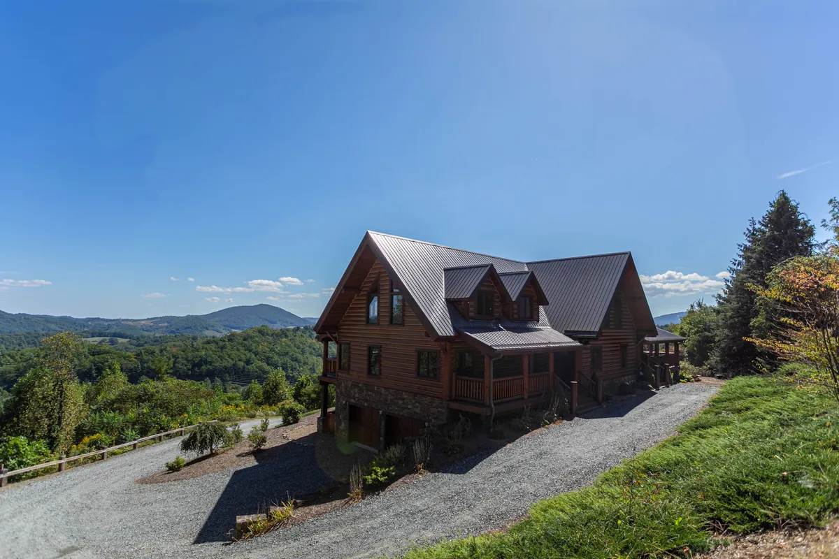 A tranquil view of the Lodge’s wooden exterior, nestled within lush greenery, with sweeping mountain vistas in the background. The porch and surrounding landscape invite outdoor gatherings, while the mountain view reinforces the property’s secluded, natural setting.