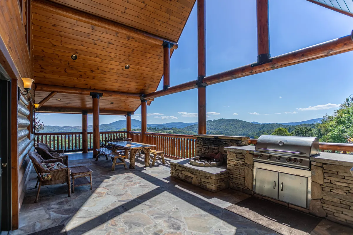 An expansive covered deck with a wooden dining table, outdoor grill, stone fireplace, and sweeping mountain views. Designed for alfresco dining and group celebrations, the space is sheltered for year-round enjoyment.
