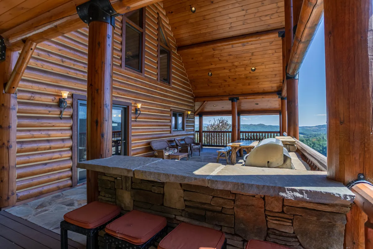 A broad view of the lodge’s outdoor seating area, highlighting the log cabin architecture, a stone bar perfect for socializing, and comfortable seating with views of the surrounding landscape. The setting is ideal for group activities, casual meetings, or unwinding after team-building exercises.
