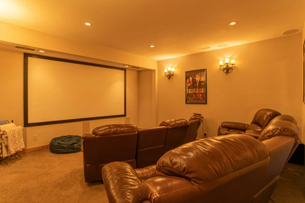 A dedicated theater room with a large projector screen, plush leather seating, and ambient wall sconces. The setting is perfect for immersive movie nights or watching the big game with friends and family.
