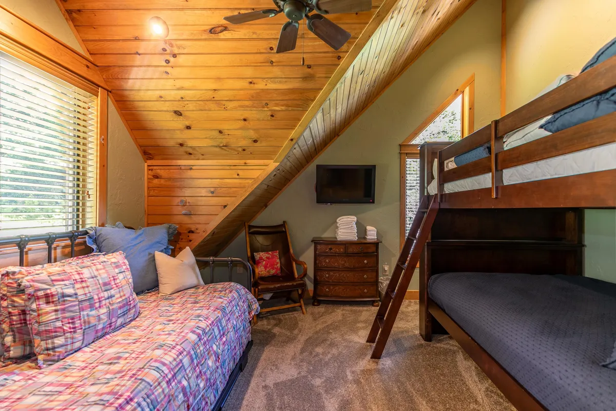 A playful, versatile room with a bunk bed, a daybed, a wooden ceiling, TV, and a comfortable armchair. The space feels casual and family-friendly, ideal for kids or flexible sleeping arrangements.