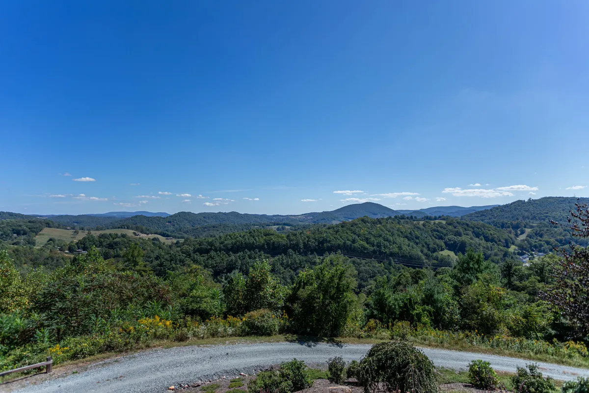 A breathtaking panoramic view of rolling hills and distant Blue Ridge Mountains under a clear blue sky, inviting exploration and outdoor adventure. The landscape is lush and expansive, instantly evoking the spirit of hiking, bird watching, and nature photography.