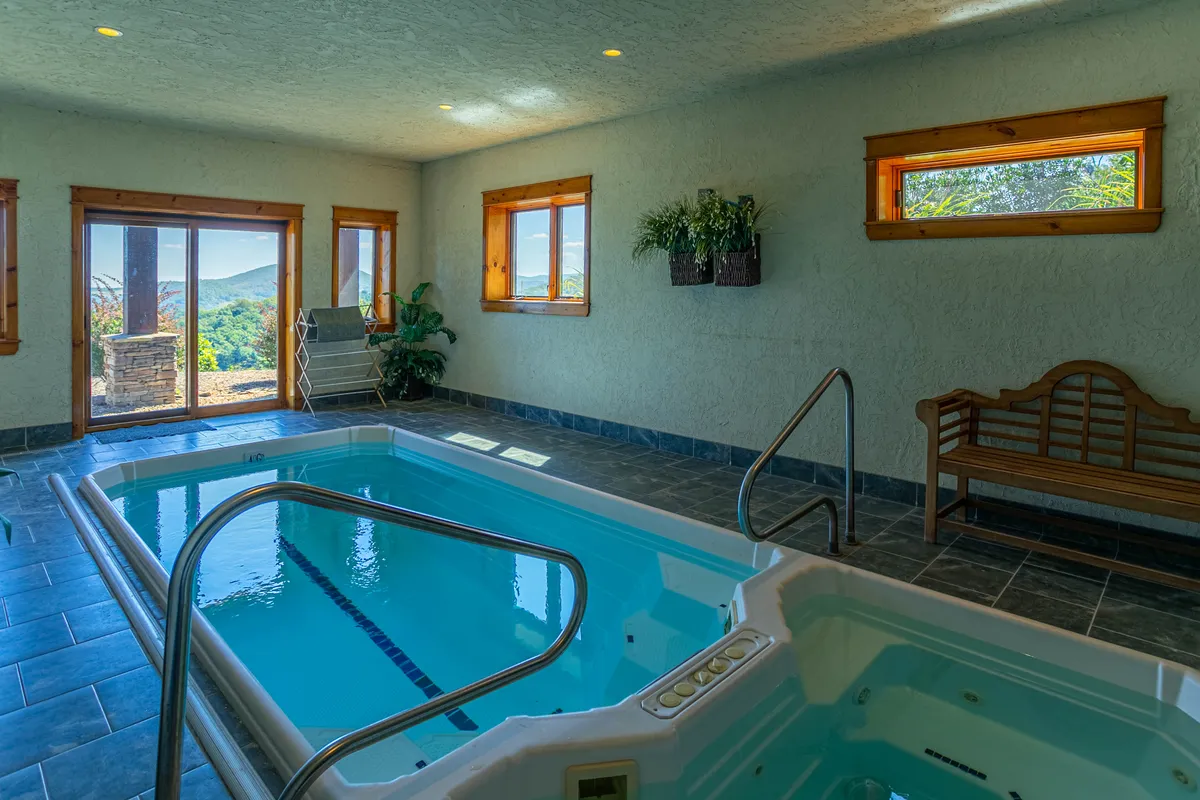 A serene indoor pool area with expansive windows letting in natural light, a wooden bench for relaxation, and tranquil surroundings. The swim spa environment promises rejuvenation and downtime after a day of activity.