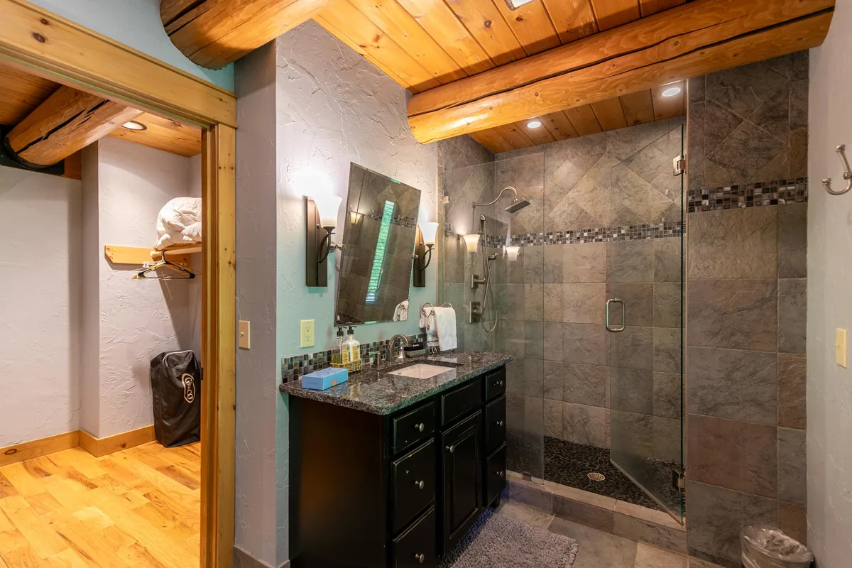 A spa-inspired bathroom with a spacious shower enclosure, a vanity with a mirror, and exposed wooden beams. The mood is calm and rejuvenating—perfect for indulgent self-care and morning routines.